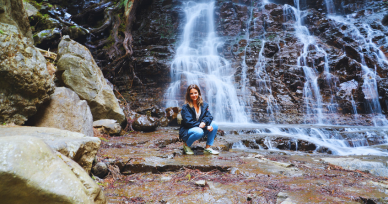 Woman standing in front of Haha no Shirataki waterfall near Mt. Fuji, posing for a peaceful portrait in nature.