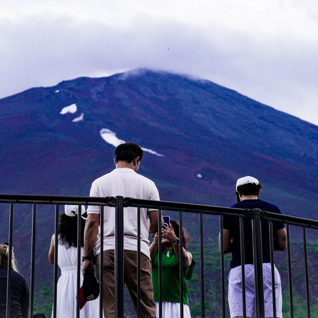 Back view of tour guests standing at Mt. Fuji’s 5th Station, surrounded by mountain scenery and clouds.