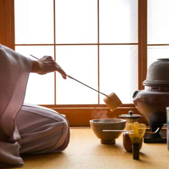 A host preparing green tea with traditional utensils during a Japanese tea ceremony.
