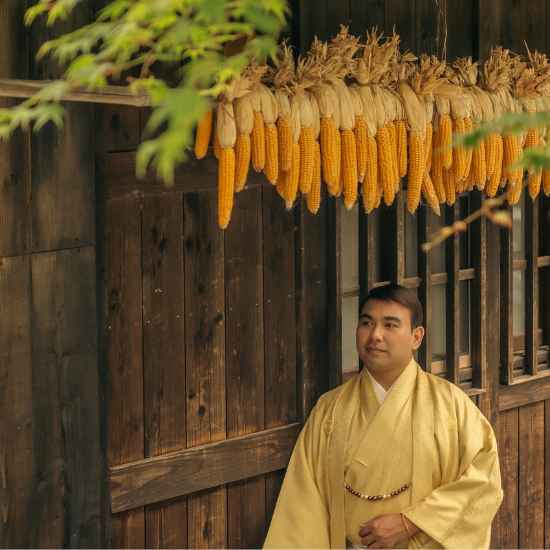 A man in a traditional kimono standing in front of a thatched-roof house at Saiko Iyashi-no-Sato Nenba.