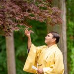 A male tour guest wearing a yellow kimono looking at red autumn leaves